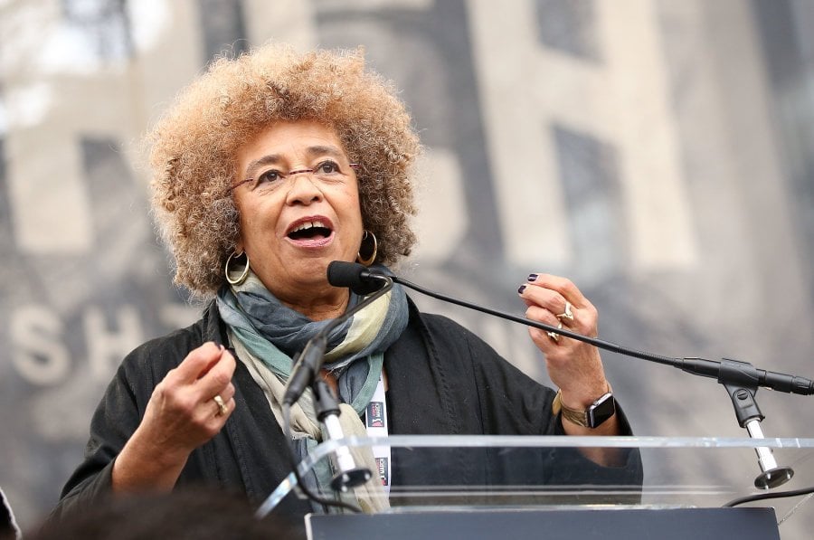 Angela Davis- mulher idosa negra- vestino casaco preto e óculos de grau- durante um discurso