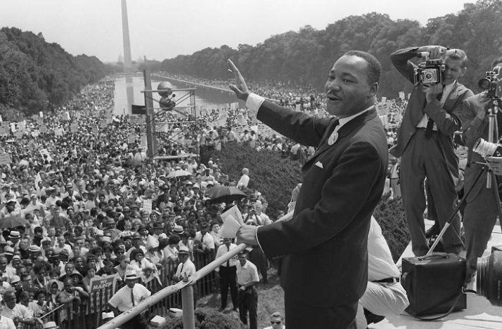 Martin Lither King Jr- homem negro, de pouco cabelo, vestindo terno e gravata- acena a seus seguidores que o acompanhava na marcha de Washington onde fez o seu mais famoso discurso 28.ago.1963