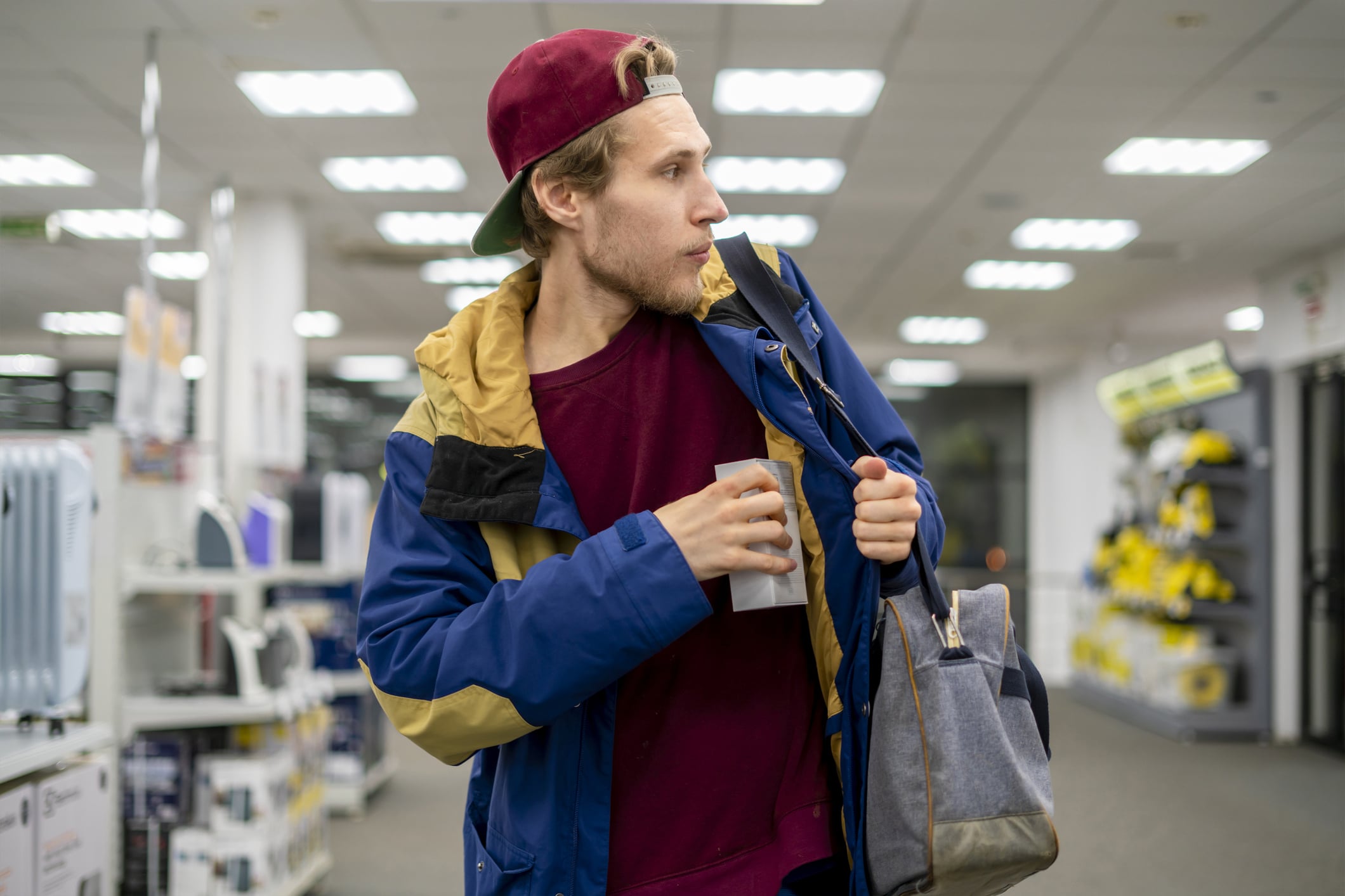 Foto de um homem branco roubando um produto no mercado e escondendo dentro da jaqueta