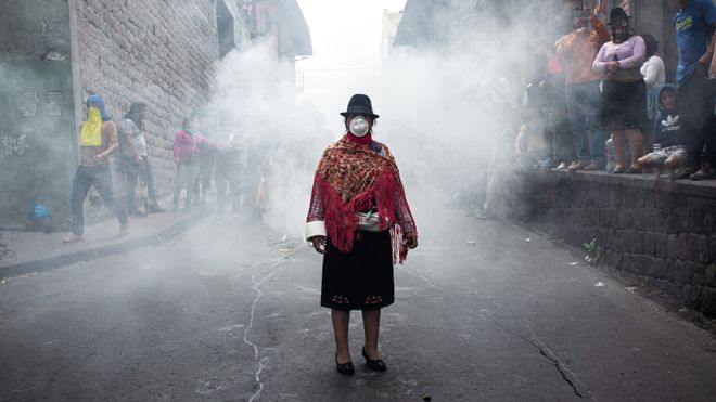 Foto de uma mulher encapusada, de pé durante o protesto