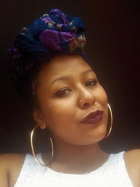 Débora Dias - mulher negra, usando turbante azul e brincos de argola.