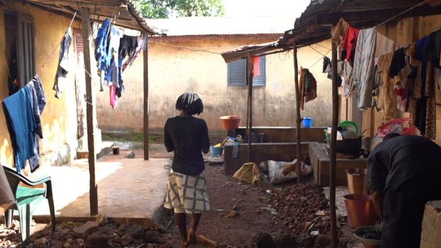 imagem de uma mulher em um quintal de barro e varias roupas penduradas no varal