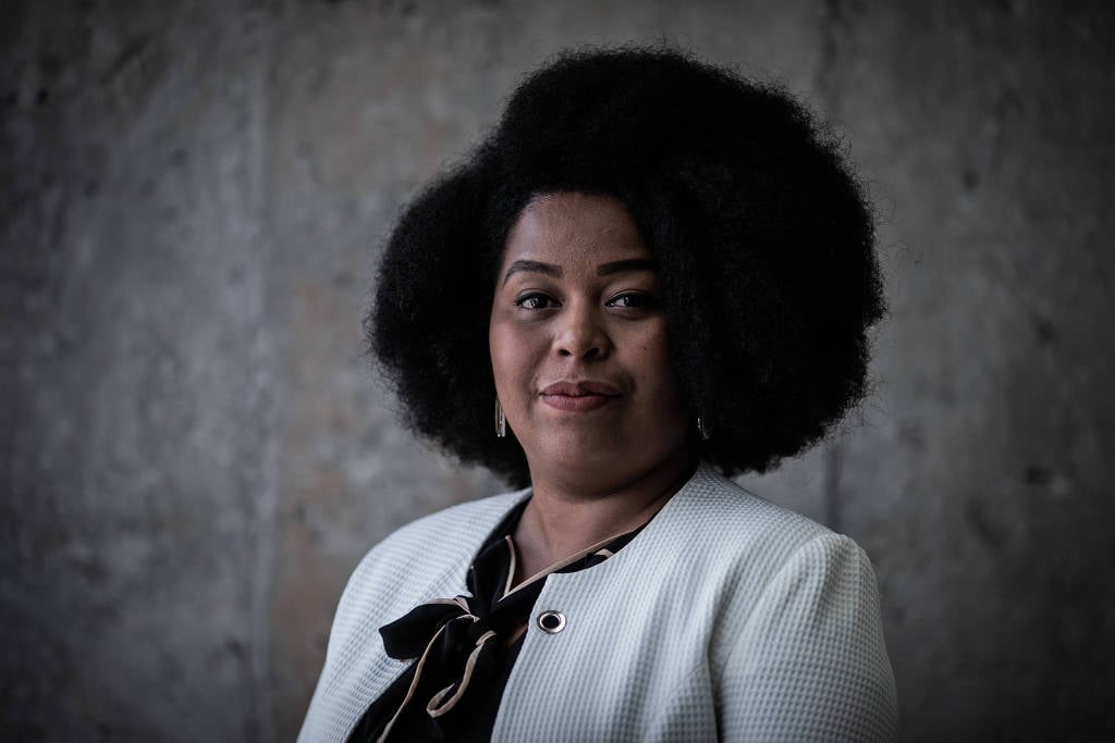 Silva Souza - mulher negra de cabelo black, usando terninho branco - em pé.