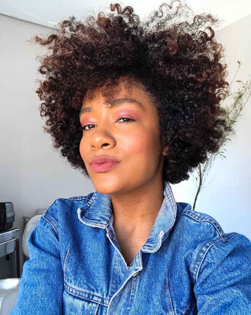 Selfie de Sah Oliveira- mulher negra, de cabelo crespo, usando camiseta jeans.