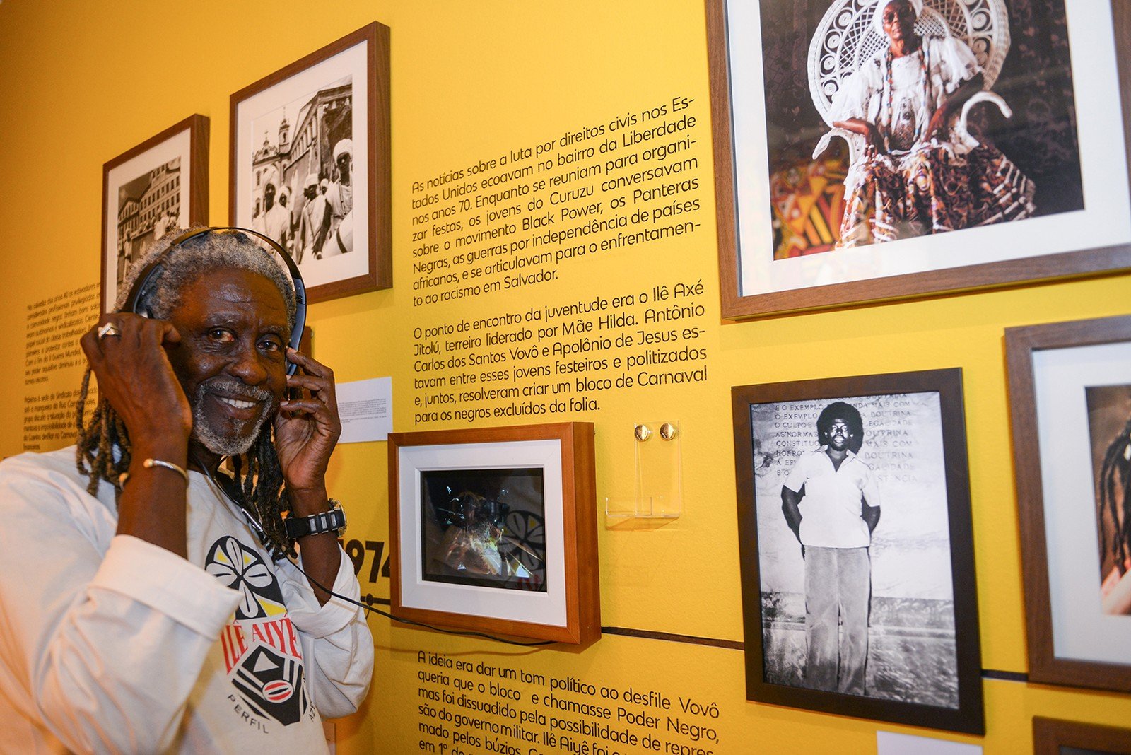 Vovô do Ilê- homem idoso negro, de dreads grisalho, usando fone de ouvido- em pé sorrindo