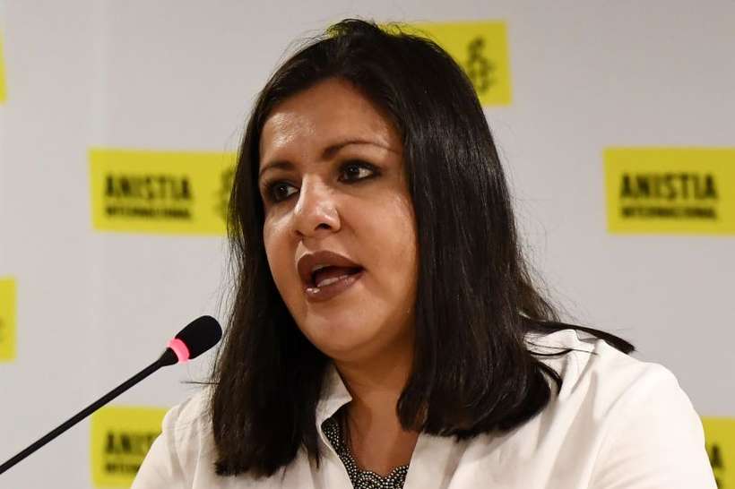 Erika Guevara Rosas- mulher branca, de cabelo preto, vestindo camiseta branca- sentada discursando na frente de um microfone