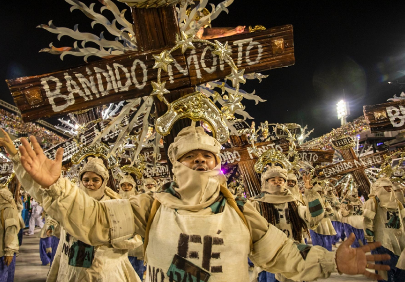 Mangueira desfila na Sapucaí - pessoas vestida com roupas escrito fé e carregando uma cruz escrito "Bandido morto"