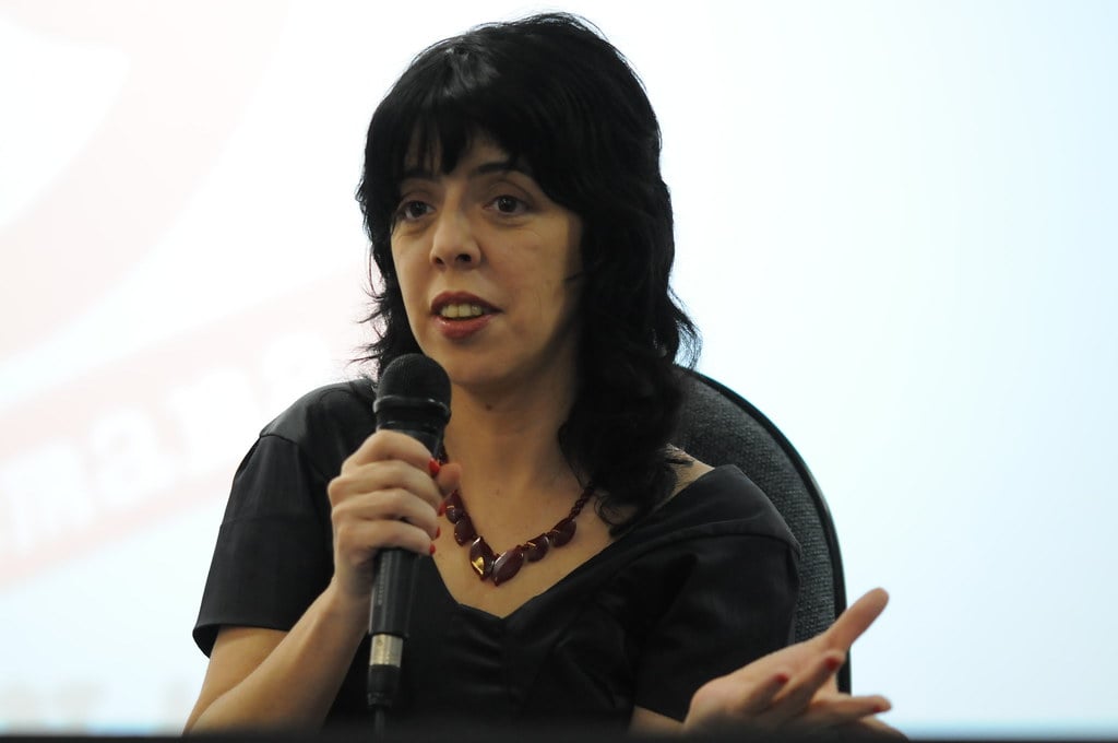 Nina Lemos, mulher branca, cabelo preto, falando no microfone. Autora dessa matéria sobre caso de Racismo